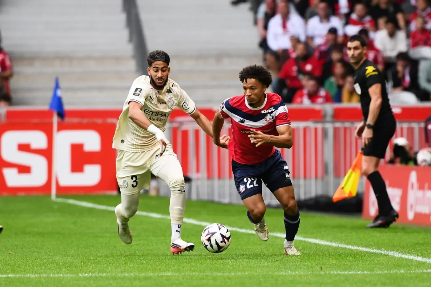 Tiago Santos carries the ball alongside a Troyes opponent, with an assistant referee behind them