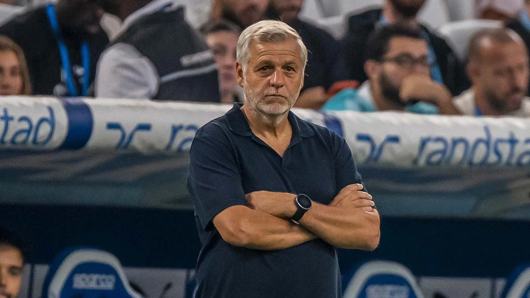Bruno Genesio stands beside the Marseille dugout with his arms crossed in OM's PSG match coverage